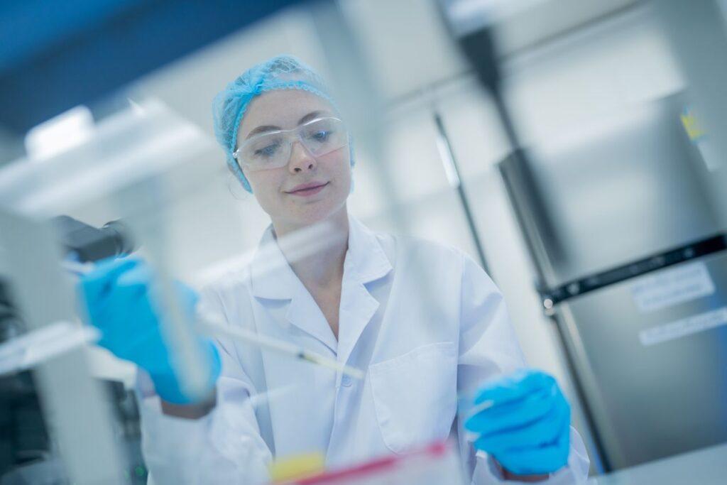 Laborantin arbeitet unter Reinraumbedingungen mit Pipette und schuetzt Proben bei der Reinraumreinigung in der Biotechnologie